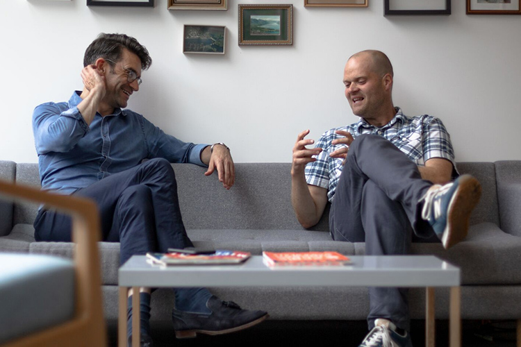 cxpartners' co-founders, Richard and Giles, sharing a laugh while sitting on a sofa in the cxpartners office.