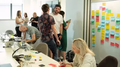 A photo of 8 colleagues in a room writing on post it notes and discussing as part of a workshop