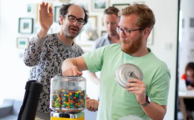 Ollie taking a handful of sweets from the office sweet jar. Another team member is pretending to push his hand away