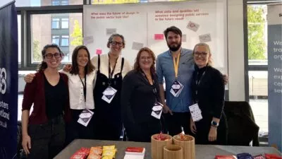 Megan, Nicola, Hannah, Amanda, Mark and Chloe with lanyards around their necks, standing at a stall at the SDinGov conference.