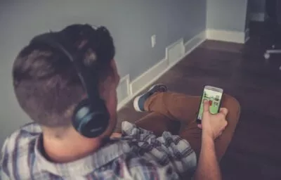 A photo of a man with headphones on looking at his phone selecting an audiobook to listen to