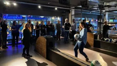 A photo of a group of people bowling at a bowling alley. It's dark outside