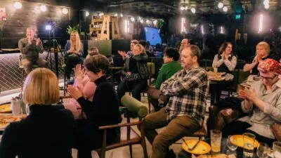 A photo of 14 people sat clapping at the UX Brighton Mentorship Closing Party