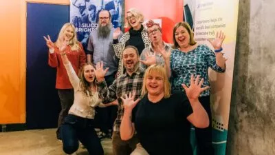 A photo of 7 people with their hands up, smiling. Julia, Kate and Sharon are on the right