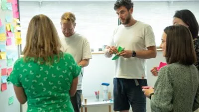 Photo of a small group of people in an office writing post it notes and sticking them to a board