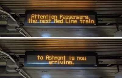 Photo of a digital display board at a train station that reads 'Attention passengers, the next Red Line train to Ashmont is now arriving'