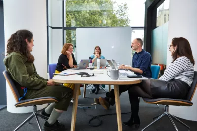 4 people sat at the table in an office setting having a meeting.